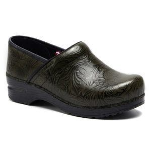 Model wearing dark green clogs standing on rustic wood floors with black cabinets in the background