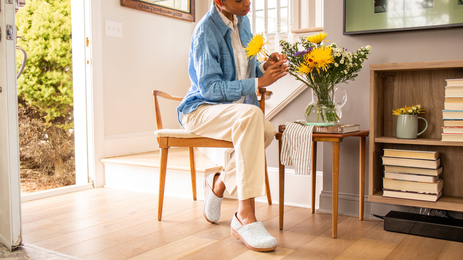 Person sitting on a chair holding flowers in a home setting