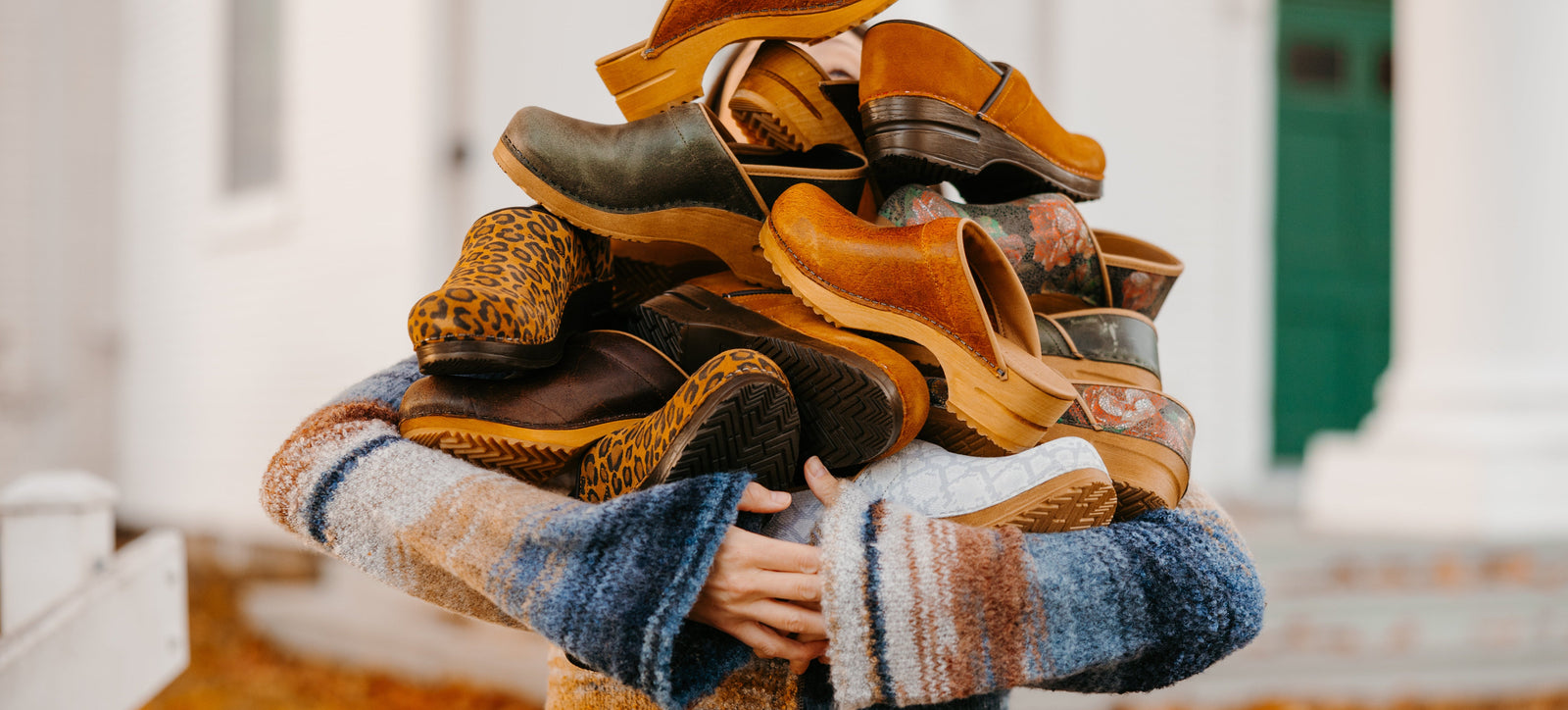 Person holding a large pile of clogs in their arms, so many so that their head is completely obscured.